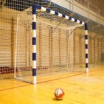 Ein Handball liegt vor einem leeren Handballtor in einer Halle.