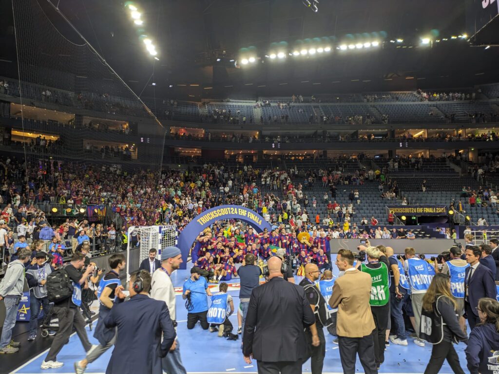 Die Mannschaft des FC Barcelona posiert auf dem Siegerpodest gemeinsam mit ihrem Maskottchen. Im Hintergrund sind die spanischen Fans zu sehen.