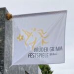Auf dem Bild ist eine weiße Flagge mit dem Logo der Brüder Grimm Festspiele. Auf dem weißen Hintergrund sind in gelb die Umrisse eines Einhorns zu erkennen. Darunter steht in Schwarzer Schrift "Brüder Grimm Festspiele Hanau"